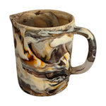 The Arila Jug is a ceramic pitcher with a marbled brown, beige, and cream pattern. It has a handle and spout, making it ideal as a table centerpiece.