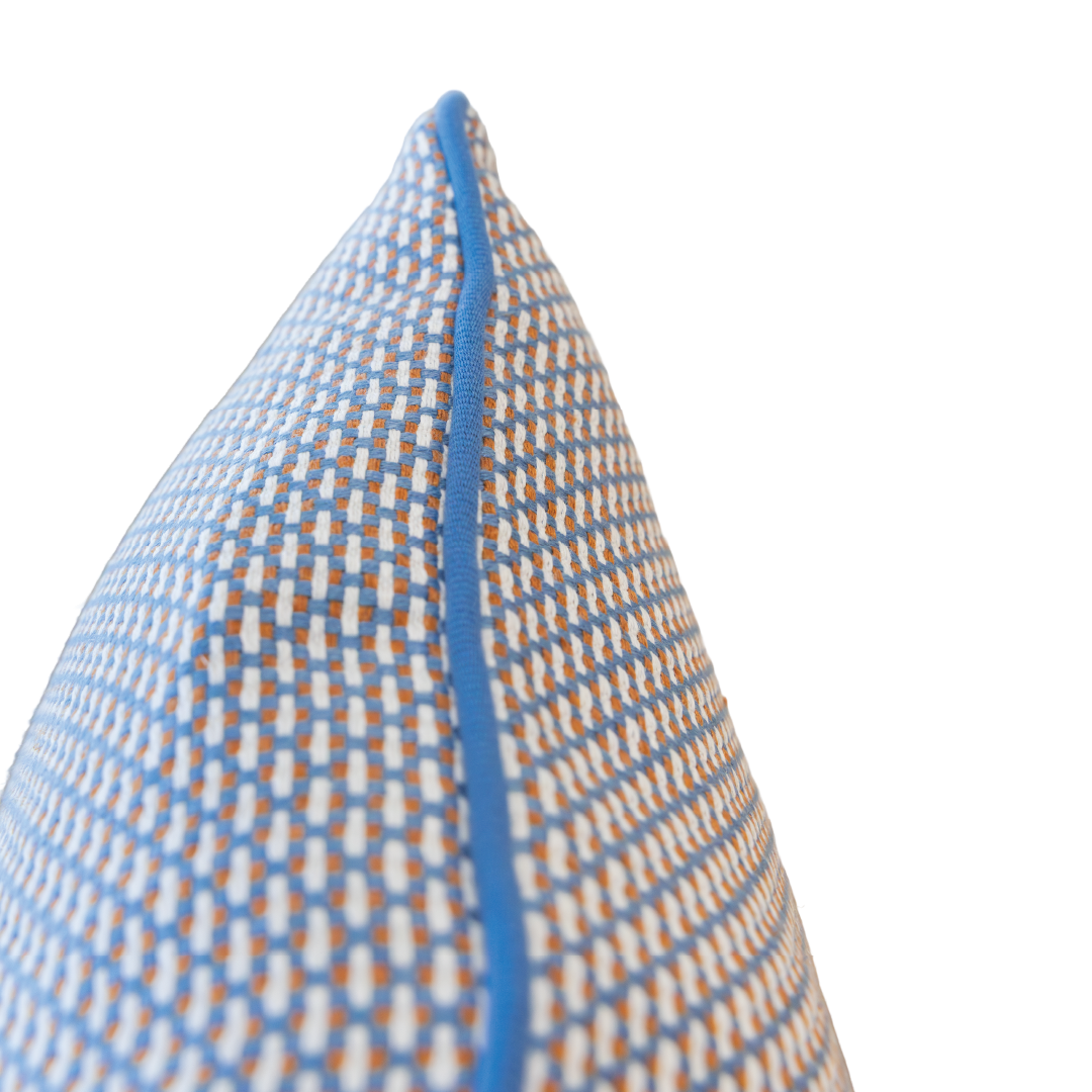 Close-up of the Arles Paon Outdoor Lumbar Pillow, featuring a blue, orange, and white pattern with blue piping, shown from a side angle against a white background. This pillow highlights vibrant colors and expert craftsmanship—an ideal choice for adding a stylish touch to your space.