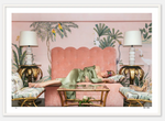 A person wearing a green outfit is lying on a pink couch in the Colony Hotel, Palm Beach, surrounded by Nick Mele Fine Art Nap Time-themed decor, including palm tree lamps and a wall mural featuring birds.