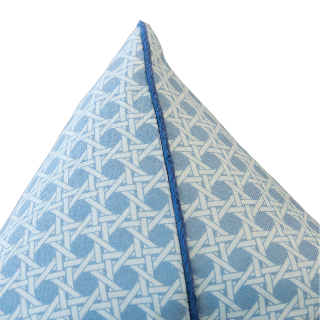 Close-up of a 22" x 22" Cane Mineral Pillow corner, featuring a geometric white lattice pattern and blue piping, filled with 100% down and set against a white background.