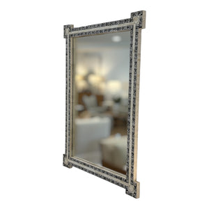 The U645 Ebony Penwork Mirror is a rectangular decorative wall mirror with a patterned frame, reflecting a softly blurred living room scene with furniture and lamps.