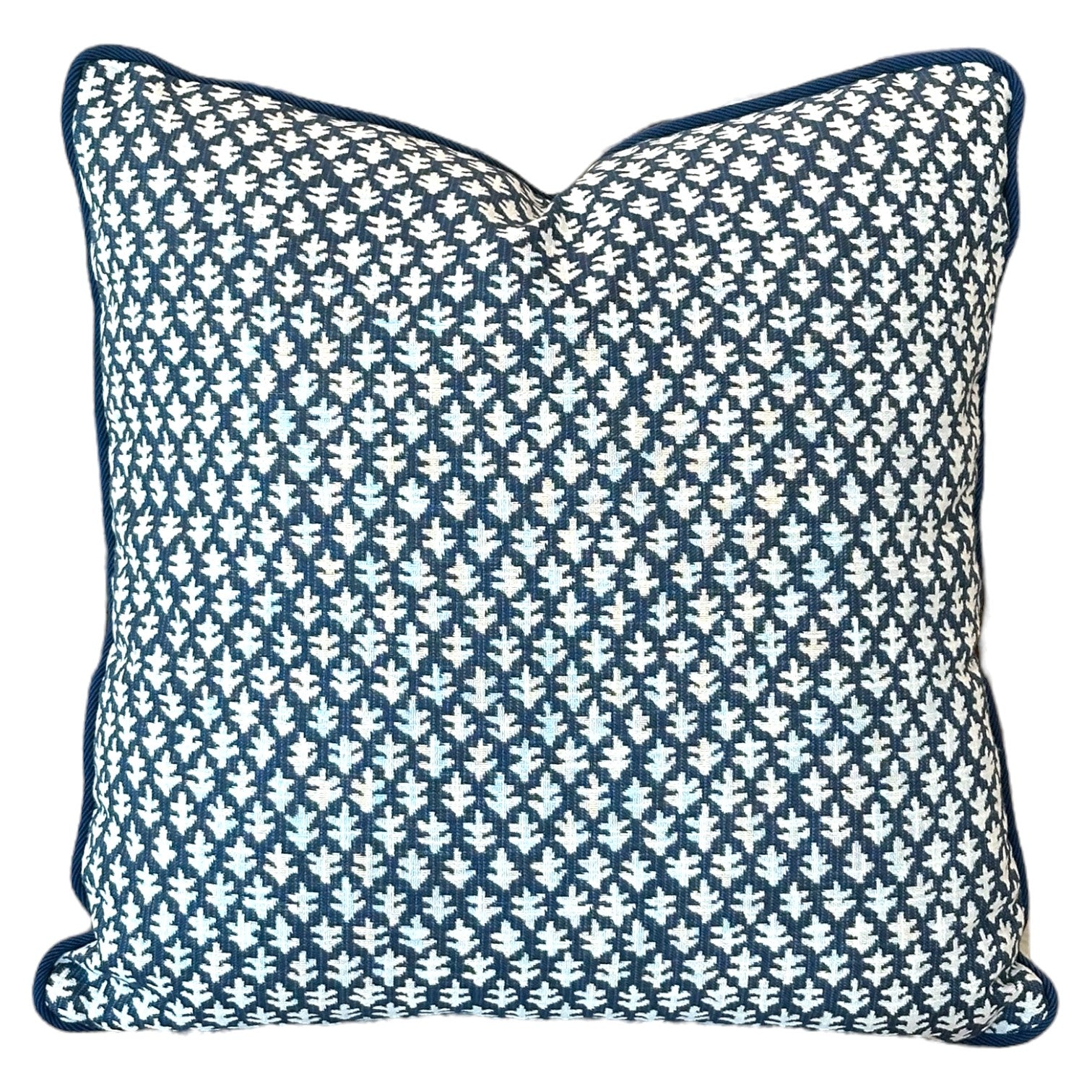 The Burma Indigo Outdoor Pillow is a handmade square pillow featuring a blue and white geometric leaf pattern and blue piping along the edges, crafted from the finest materials.