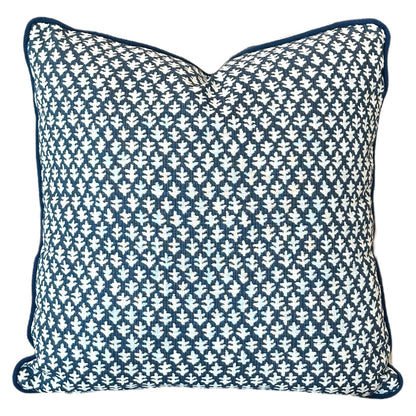 The Burma Indigo Outdoor Pillow is a handmade square pillow featuring a blue and white geometric leaf pattern and blue piping along the edges, crafted from the finest materials.