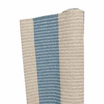 A close-up of the Amy Stripe in Medium Blue, a handwoven rug with beige and blue vertical stripes, partially rolled on one end against a white background—designed for versatile indoor or outdoor use.