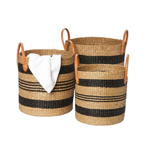 The Hudson Basket Collection features three woven baskets with black stripes and leather handles—one holding a folded white cloth—adding style to your home décor against a plain white background.