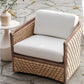 The Capitola Swivel Lounge Chair, featuring woven rattan and white cushions, sits by a small round side table on a stone patio; its powder-coated aluminum frame ensures outdoor durability.