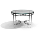 The Amalfi Glass Top Round Dining Table features a hand-forged steel frame with decorative curved metal accents on the legs and base, shown on a white surface.