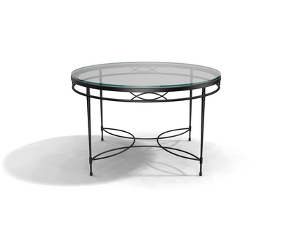The Amalfi Glass Top Round Dining Table features a hand-forged steel frame with decorative curved metal accents on the legs and base, shown on a white surface.