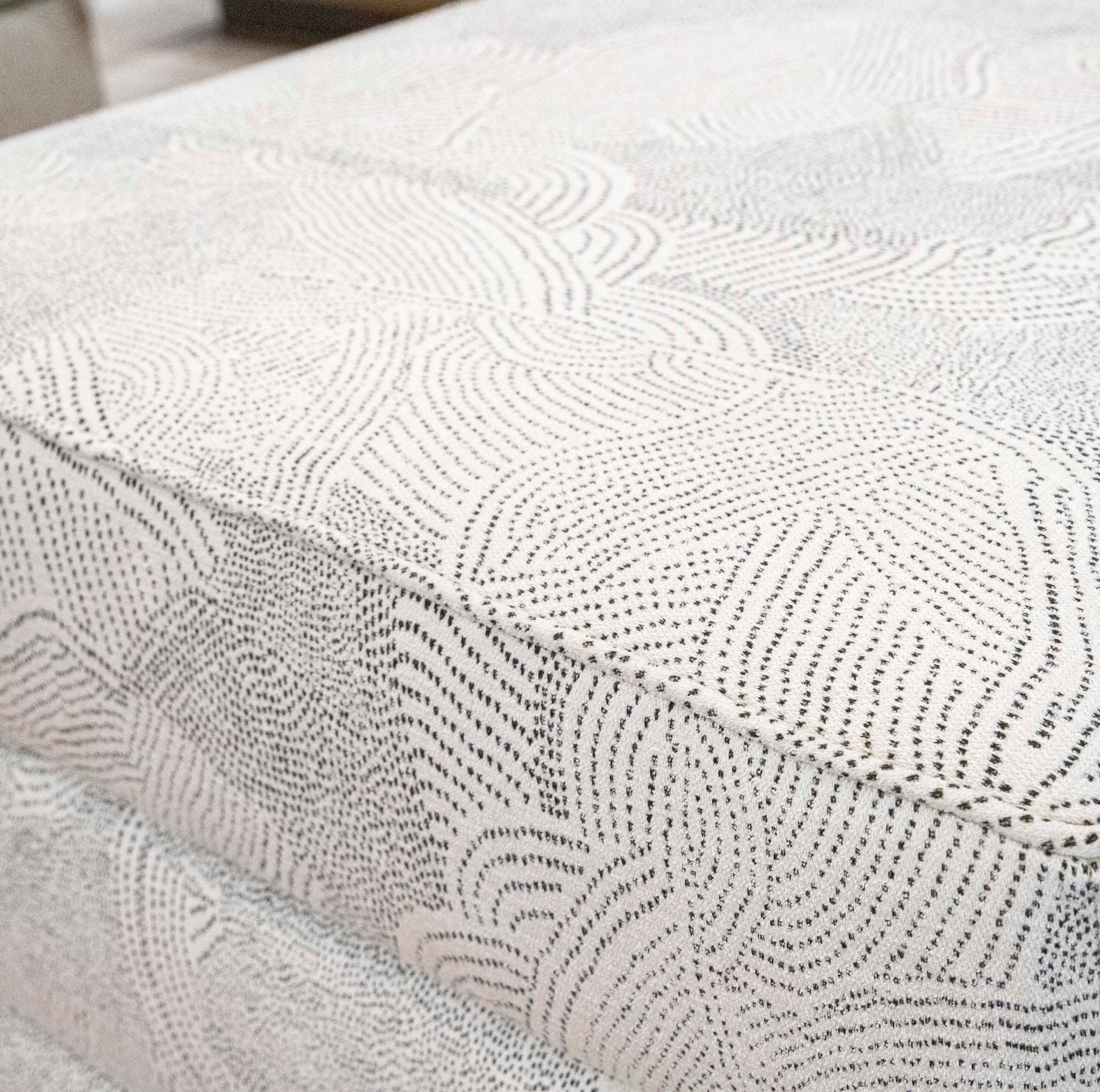 Close-up of a textured fabric with dotted and wavy patterns in a light color, ideal for covering a custom Channeled Ottoman.