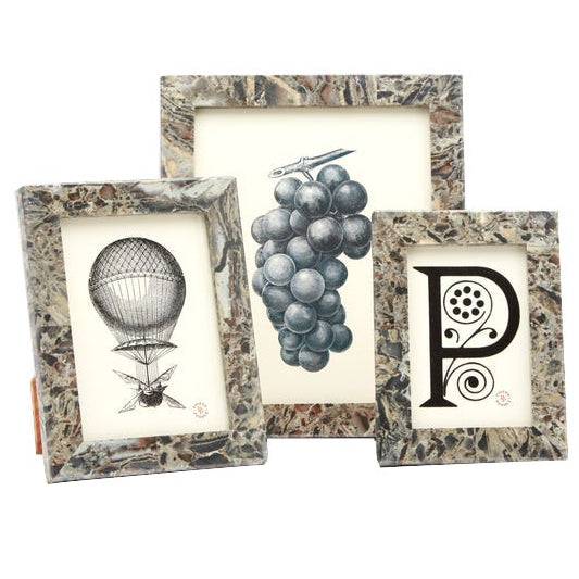 The Corsica Frame Collection features three decorative frames with a marble pattern, showcasing black and white illustrations of a hot air balloon, grapes, and the letter "P" with floral accents.