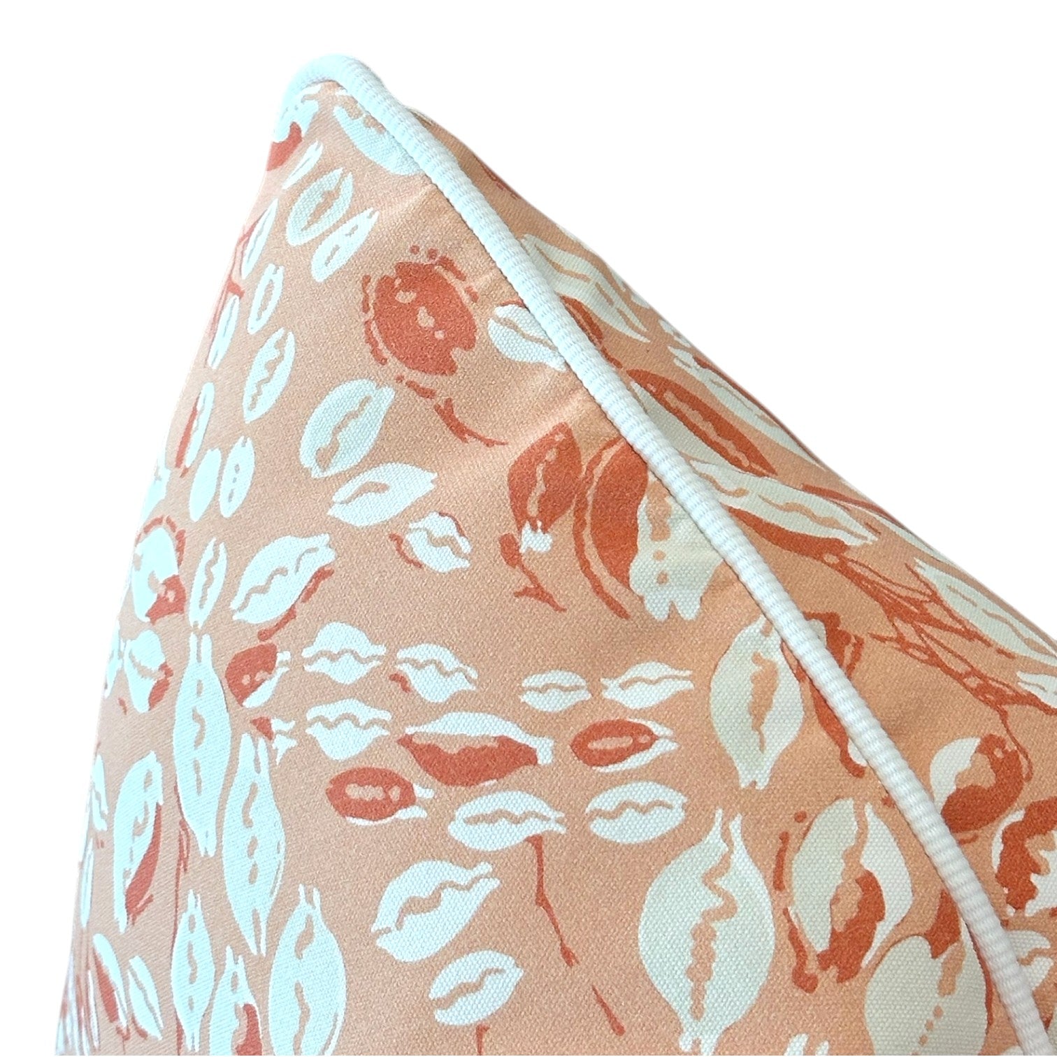 The Cowrie Shell Coral Outdoor Pillow features a peach and white seashell and leaf pattern with white piping. Crafted from premium materials, this custom-made pillow brings coastal charm to any setting.