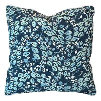 The Cowrie Shell Navy Outdoor Pillow features a dark blue background with a leafy pattern in light blue, green, and white, crafted from premium materials for lasting comfort.