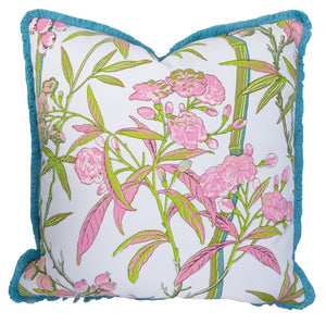 The Enchanted Garden Bamboo Outdoor Pillow features a floral pattern with pink flowers and green leaves on a white background, accented by blue fringe. Made from premium materials, it offers exceptional craftsmanship and style for your outdoor space.