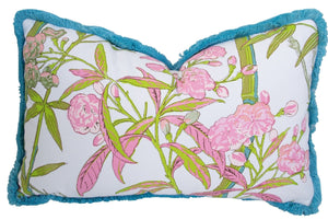 The Enchanted Garden Bamboo Outdoor Lumbar Pillow features a custom rectangular design with a blue fringe border and a floral pattern of pink flowers and green leaves on a white background.
