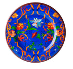 Part of the Mario Luca Giusti Pancale Blue Collection, this vibrantly painted melamine dinner plate features a blue background adorned with striking orange, red, and white floral patterns.