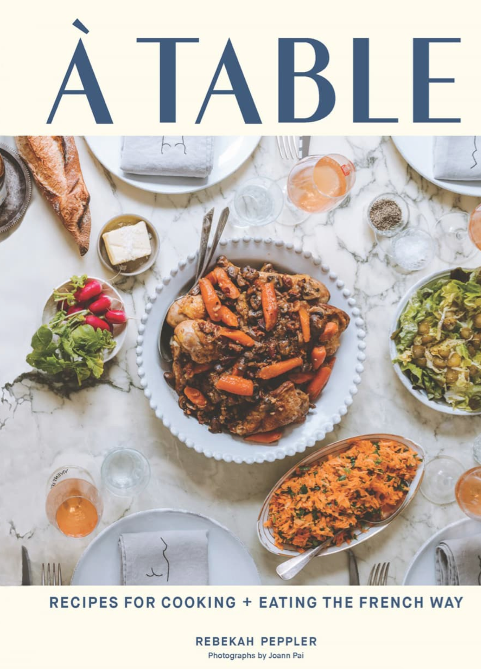 Cover of the book "A Table: Recipes for Cooking and Eating the French Way" by Rebekah Peppler, featuring French recipes like roasted meat and vegetables, shredded carrot salad, a baguette, and bowls of greens on a marble table.