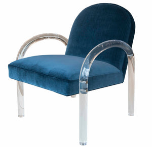 The Elva Acrylic Arm Chair is a modern piece with a blue cushioned seat and backrest, featuring transparent, curved acrylic arms and legs.