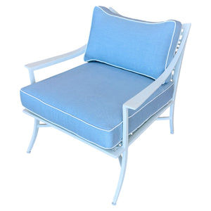 The Haret Outdoor Lounge Chair features a sleek white metal frame and blue cushions with white piping, making it a stylish addition to any contemporary patio.