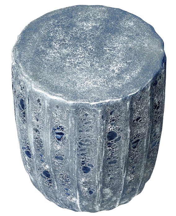 The Uriah Stool features a blue reactive ironstone finish with a cylindrical form, textured surface resembling stone, and distinctive scalloped edges.