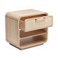 The Marsh Bedside Chest is a light wood bedside chest with rounded edges, an open lower shelf, and a single upper drawer featuring a blonde rattan front and two handles.