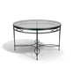 The Amalfi Glass Top Round Dining Table features a hand-forged steel frame with decorative curved details, creating a striking shadow on a white background.