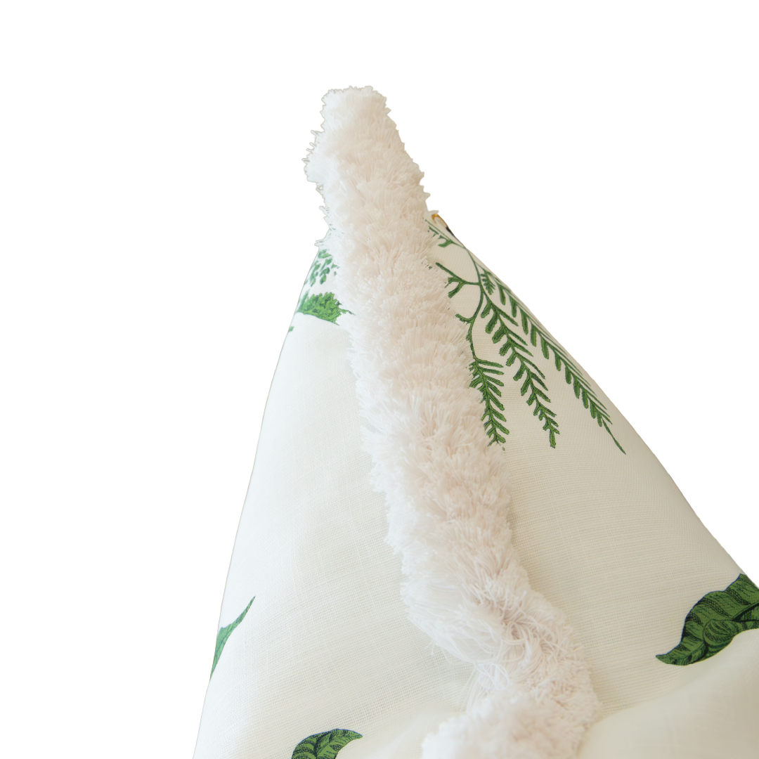 A close-up of the Woodland Fern Outdoor Pillow, featuring green fern leaf patterns on a white background with a fluffy white trim and a hidden zipper closure.