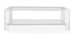 The Surrey Acrylic Rectangular Cocktail Table features a clear acrylic frame, rectangular glass top, and lower glass shelf, bringing a modern accent to your contemporary living space. Shown against a white background.
