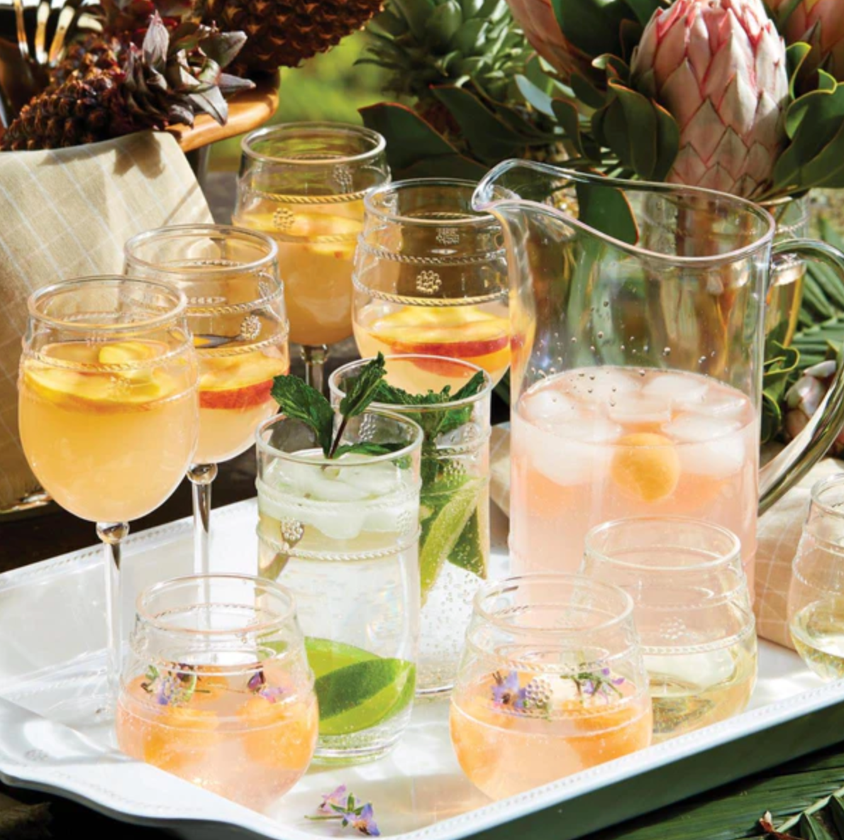 Experience a delightful array of summer cocktails and refreshments served in bohemian-style glasses from the Juliska Isabella Acrylic Collection. This ensemble, neatly arranged on a tray, features vibrant slices of citrus fruits, a stylish pitcher, and garnishes such as mint leaves and edible flowers—ideal for the adventurous entertainer.