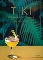 A cocktail glass with a tropical drink and garnishes on a yellow surface. The background features the book cover titled "Tiki: Modern Tropical Cocktails," one of the classic tiki bibles celebrating Caribbean rums and vibrant tiki drinks.