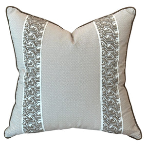The Lattice Cocoa Pillow with Tape Trim features a light beige fabric, two vertical gray and white geometric stripes, and dark edge piping. Expertly crafted, it adds an elegant touch to any space.