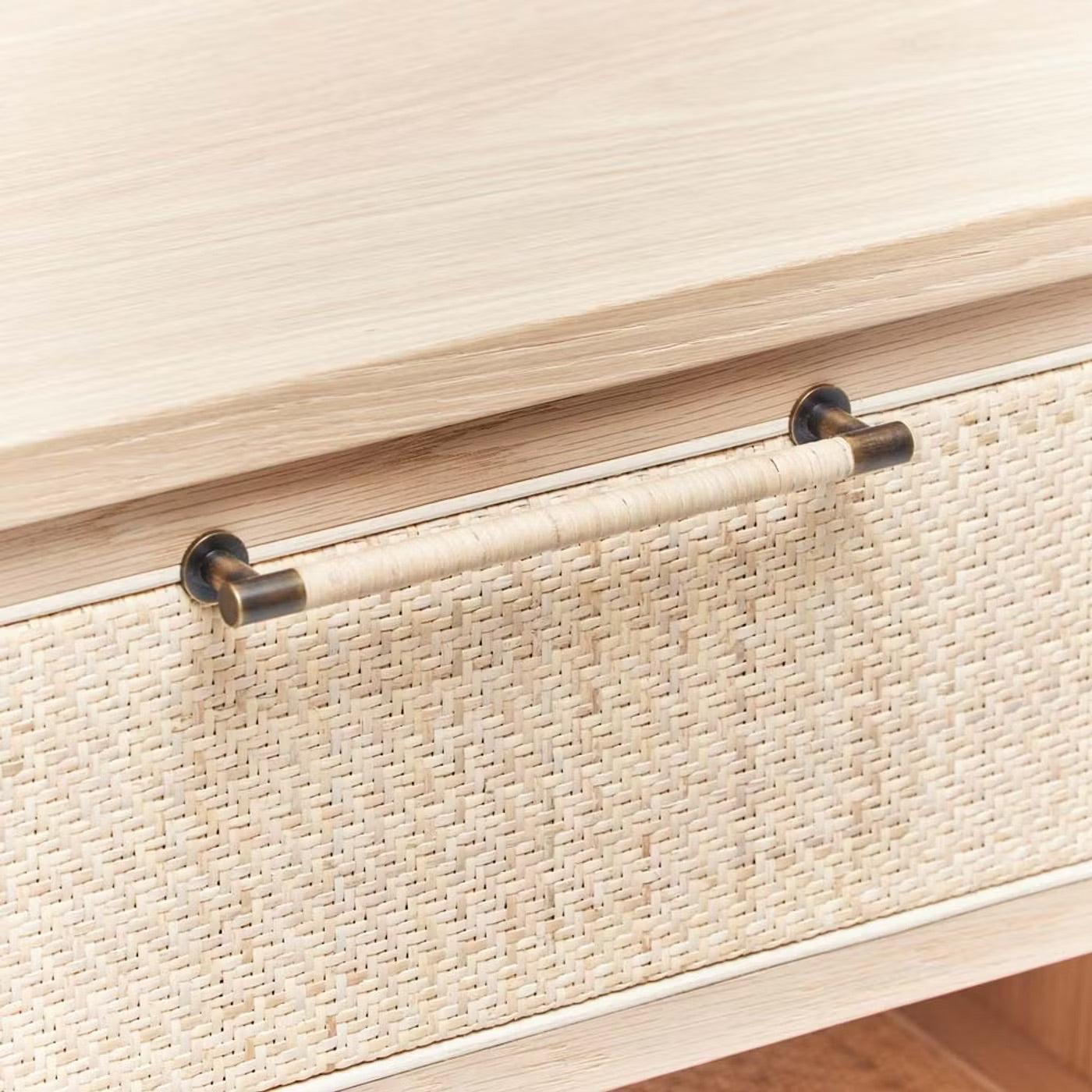 A close-up of the Marsh Bedside Chest, featuring a blonde rattan finish, textured woven front, and a cylindrical metal and wicker handle.