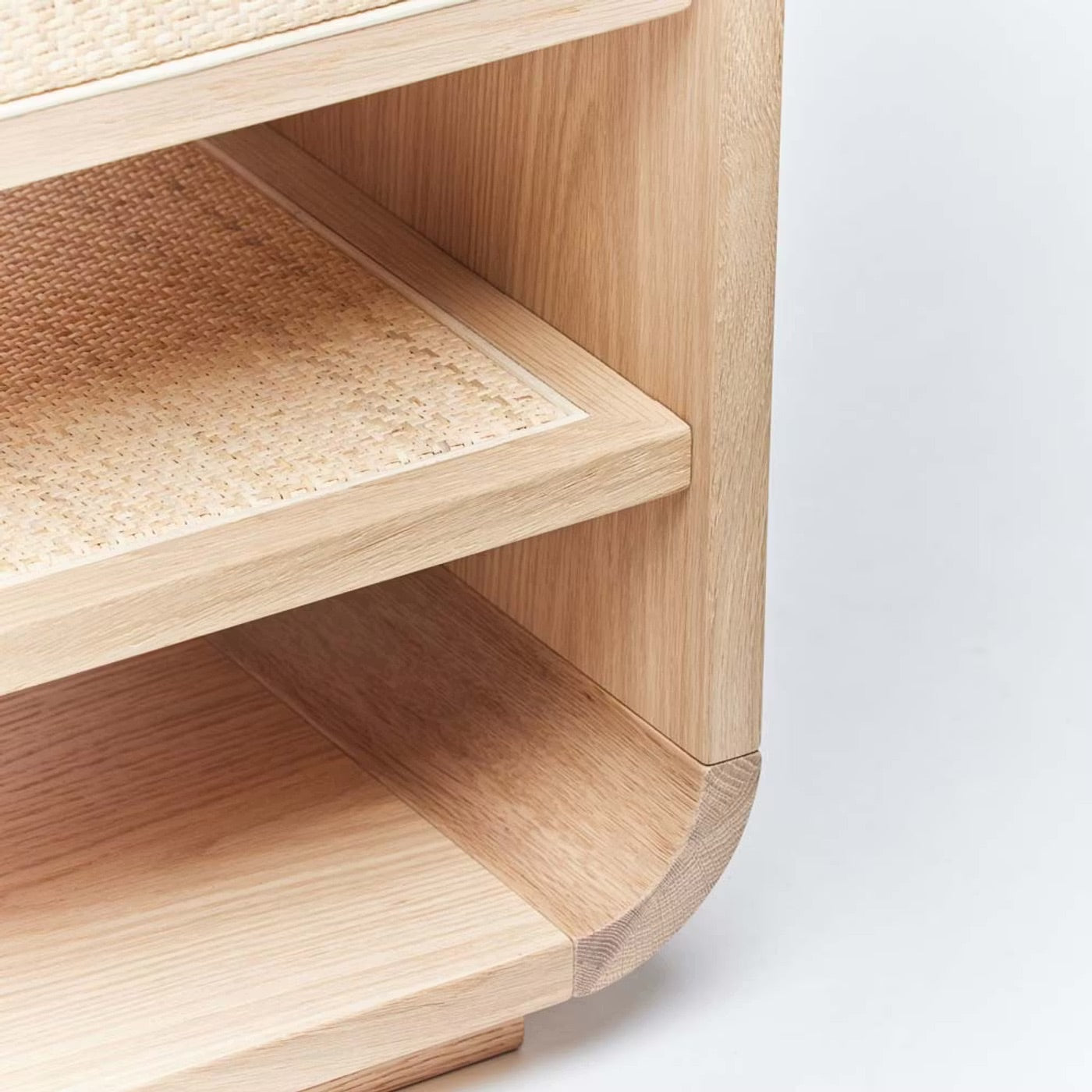 Close-up of the Marsh Bedside Chest, a wooden shelf unit with two shelves, featuring a saddle oak frame and blonde rattan detail on the upper shelf—an elegant addition to any bedside.