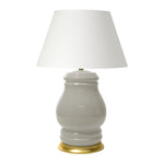 The Charleston Table Lamp in Greige showcases a glossy, curvy ceramic base with a gold-toned rim and a wide white fabric shade, creating an elegant look that adds a cozy ambiance to any room.