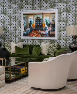 A luxe setting features a **Marquesa Sofa** in green velvet, paired with white armchairs against patterned wallpaper. A glass coffee table sits on a colorful rug beneath a large framed photograph. Two beige table lamps elegantly flank the modern interpretation of this living room.