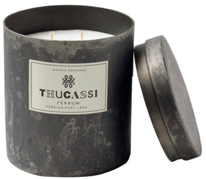 Gray decorative candle jar with a lid, labeled "Thucassi Ferrum Candle Collection, Foreign Port" and featuring three unlit wicks, exuding an enigmatic jasmine scent.