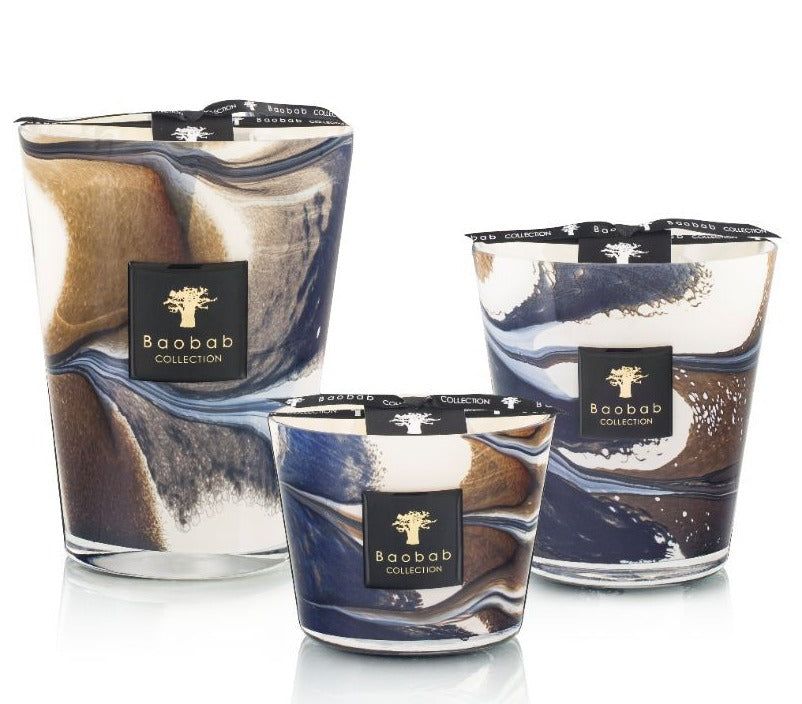 Three Baobab Collection Delta Nil candles of different sizes with swirling brown, white, and blue designs on the glass containers. Each candle has a black label with the Baobab Collection logo, evoking notes of sea salt mixed with hints of papyrus flower.