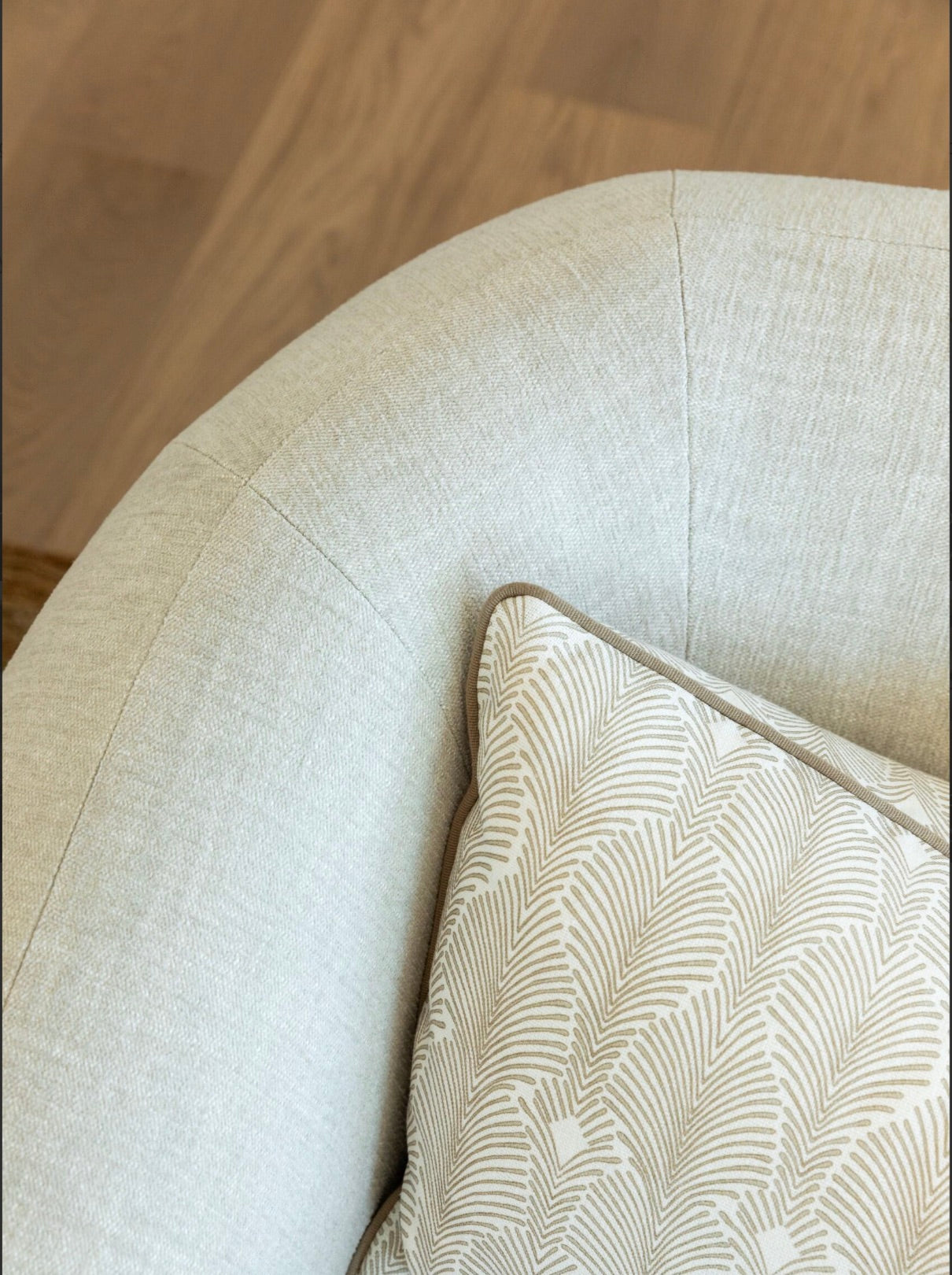 Close-up of the Obi Lounge Chair, a light beige upholstered piece from our home furnishings collection, featuring a decorative pillow adorned with a white and light brown geometric pattern. The serene ambiance is enhanced by the light wood finish of the floor beneath.