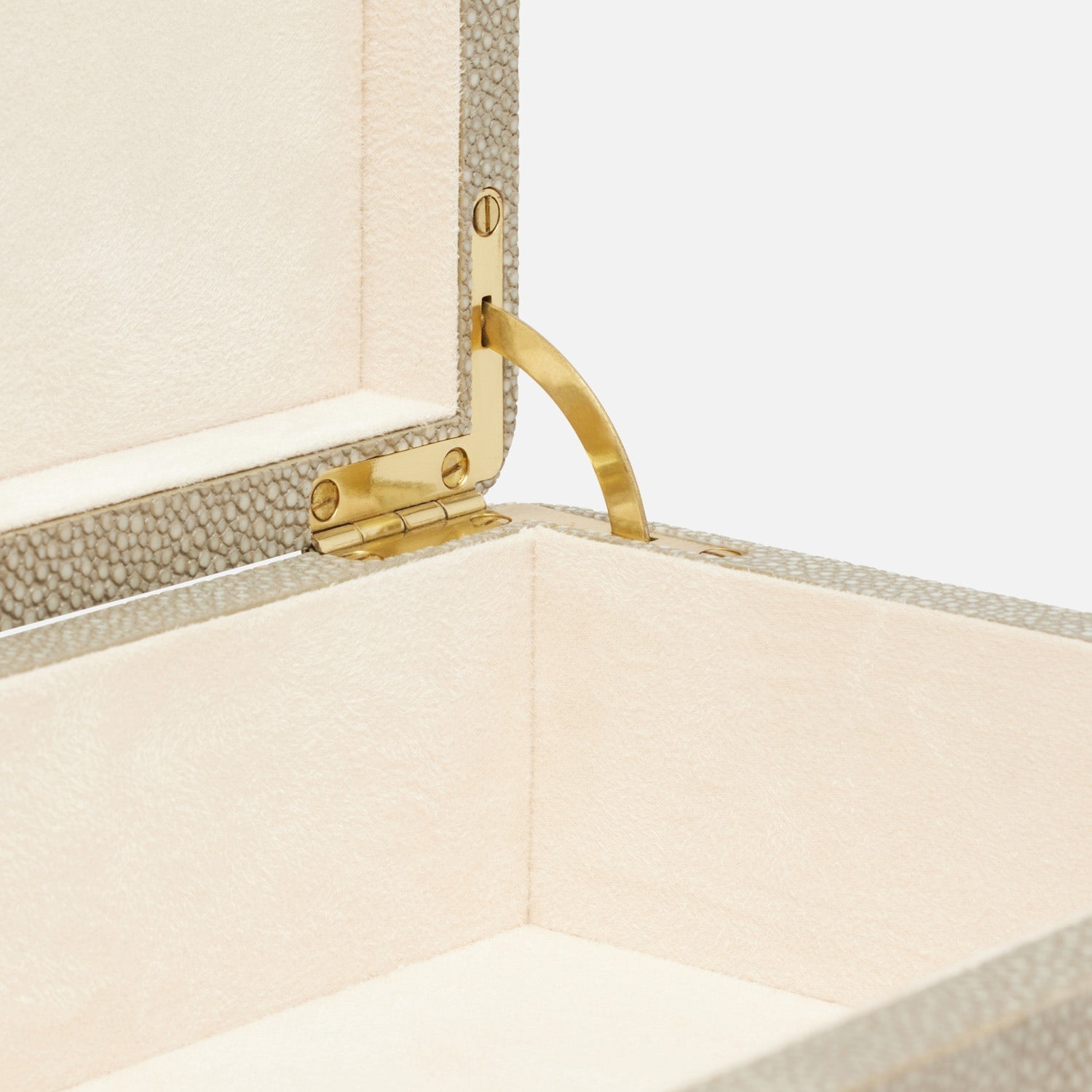 Open beige textured jewelry box with a gold hinge and cream-colored suede lining. The lid is partially lifted, revealing the box's soft interior and mechanism, showcasing its elegant design, akin to a rounded corner Kiraz Sand Shagreen Box, Small.