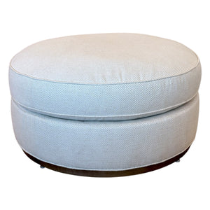The Bespoke Round Ottoman in Drummond Bone features a cushioned top and dark base, making it an ideal accent piece for any room.