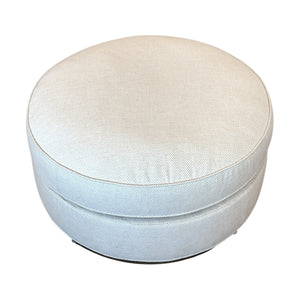 The Bespoke Round Ottoman in Drummond Bone features light beige upholstery, a smooth fabric texture, and a round design—ideal as an accent piece against white backgrounds.