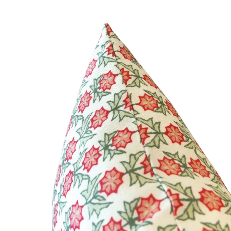 The image shows the corner of the Akhil Azalea Outdoor Pillow, featuring a weather-resistant design with a red and green floral pattern on a white background, photographed against a plain white backdrop.