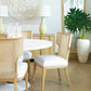 Modern dining area with light wood furniture, white cushions, a large potted plant, wall art, a tall mirror, and the Misty Country Dining Table featuring copper ring accents on its hand-turned base. Two table lamps rest on a wooden sideboard.