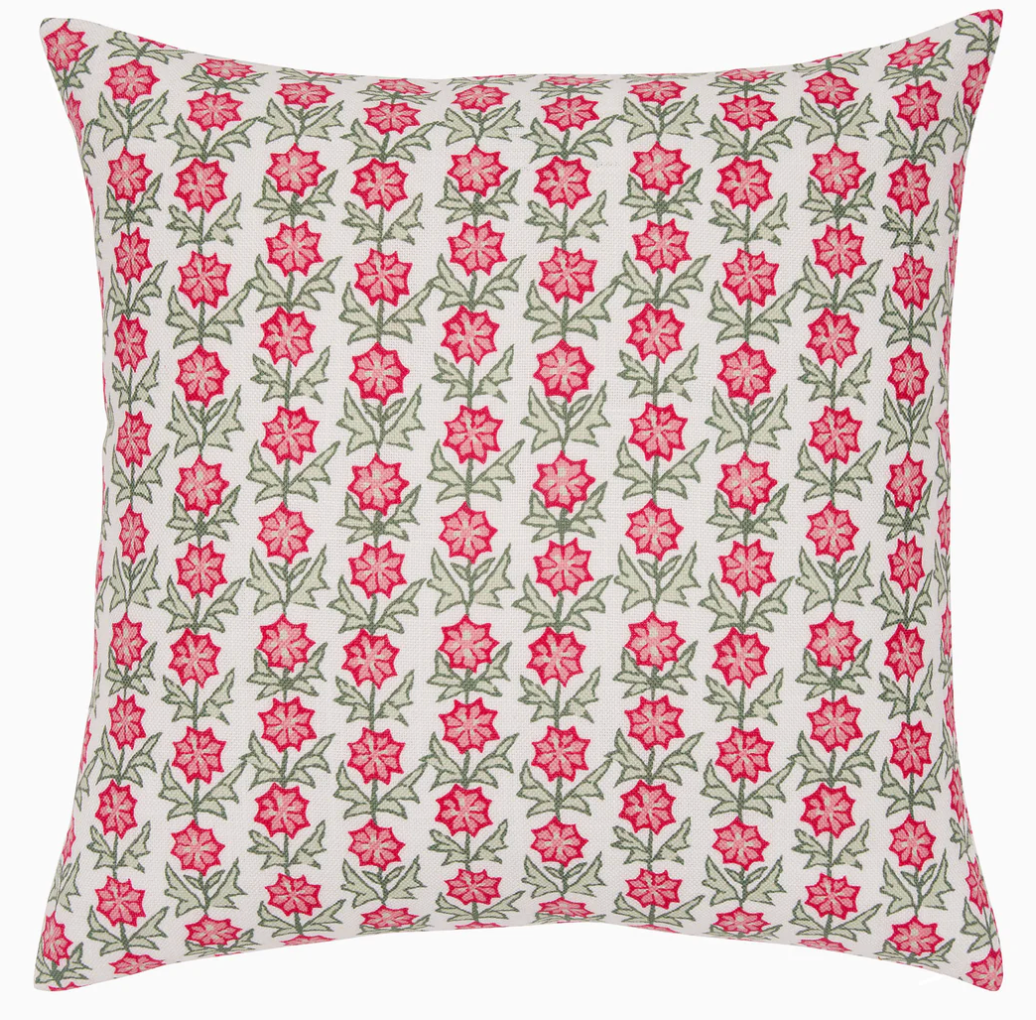 The Akhil Azalea Outdoor Pillow features a white background with a repeating pattern of pink flowers and green leaves, making it the perfect weather-resistant accent to add charm to any patio or garden space.