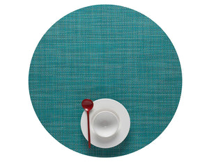 A Mini Basketweave Round Placemat in turquoise holds a white cup and saucer with a red spoon on top, viewed from above—ideal for bringing vibrant color to your dining table.