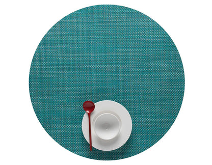 A Mini Basketweave Round Placemat in turquoise holds a white cup and saucer with a red spoon on top, viewed from above—ideal for bringing vibrant color to your dining table.