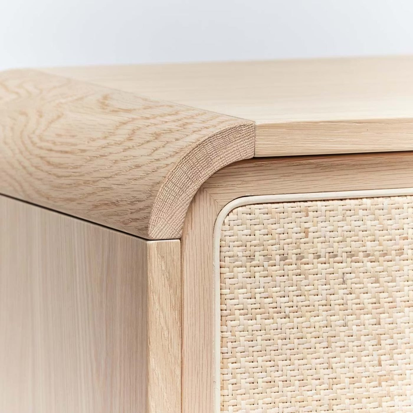 Close-up of the Marsh Bedside Chest, crafted from saddle-finished oak with a rounded edge and a door featuring a blonde rattan woven panel.