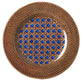 The Mario Luca Giusti Patagonia Blue Collection features a decorative plate adorned with a woven brown pattern on the rim and a blue geometric lattice design in the center, seamlessly blending modern aesthetics with timeless charm.