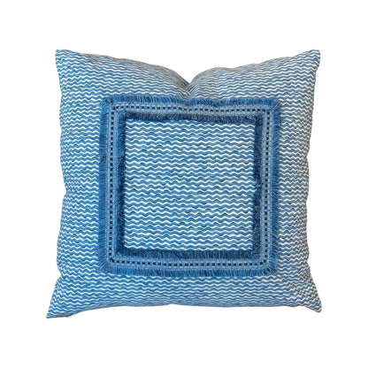 The Sky Popple Outdoor Pillow features a blue and white wavy pattern in Fermoie Popple fabric, accented with a bold blue fringed square border, displayed on a white background.