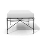 The Amalfi Ottoman showcases a minimalist design with a white cushion on a sleek, hand-forged black steel frame, displayed against a plain white background.