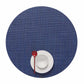 A white bowl and plate with a red spoon sit together on a large, round, textured blue Mini Basketweave Round Placemat—ideal for adding color to any dining occasion.
